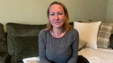 A blonde woman sits on  green velvet sofa