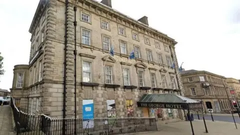 The George Hotel in Huddersfield, with its name across the front and on the entrance canopy. Blue flags fly above the entrance.