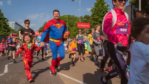 Great Bristol Run Children holding hands with adults start the Great Bristol run. Some are wearing sportswear whilst others are dressed as superheroes