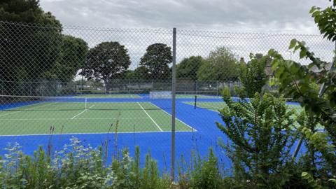 Green tennis courts on a blue foundation are framed by verdant undergrowth