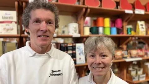 Vic and Karen Dowdey standing with rows of chocolates and wrapping behind them including love heart boxes on shelves