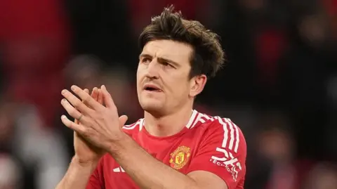 PA Media Harry Maguire in a red Manchester United shirt, he is looking to his right and clapping his hands.