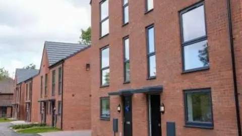 Modern red brick semi-detached properties stretch away to the left. They are between two and three stories high, and have black doors and window frames