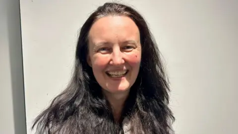 Cad Taylor / BBC A portrait of a woman close up with dark hair. She is smiling