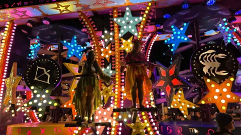 A carnival cart which features many illuminated stars. Two performers are on the cart.