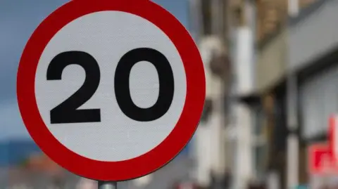 Picture of the 30mph road sign in a street. The background is heavily blurred. 