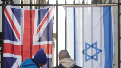 Pacemaker Two people putting up a Union Jack flag and Israeli flag on a railing.