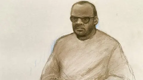 Elizabeth Cook/PA A brown and white court sketch of Simon Levy, wearing a long sleeved top and sunglasses. He has short dark hair which appears to be receeding at the top and dark skin. 