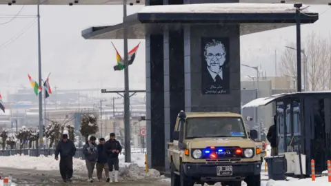 Scene at Iraqi border with Iran, as a vehicle and people pass through a crossing point in the snow