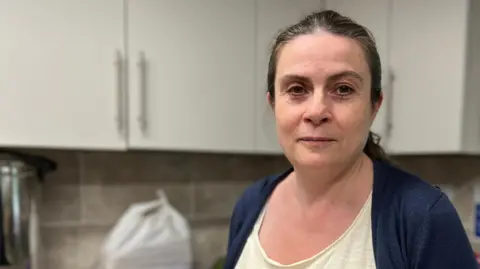 BBC Image shows Family Voice Peterborough CEO Louise Ravenscroft standing in a kitchen. In the background there are groceries in clear packaging. 