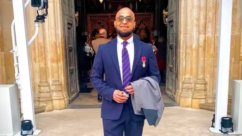 Afruz Miah Afruz wears a white shirt and blue suit. 