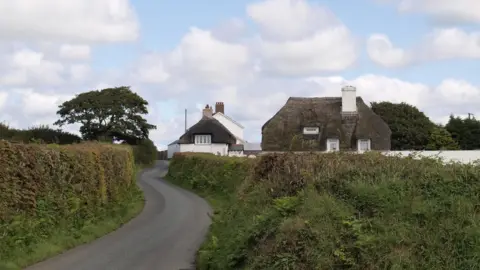 Education Images/Getty Images Small country road past thatched houses, Cornwall, UK