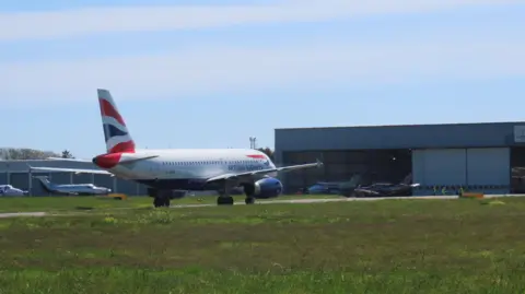 The image shows a British Airways jet on Guernsey's airfield. It is painted white with a Union Jack on the tail of the aircraft. 