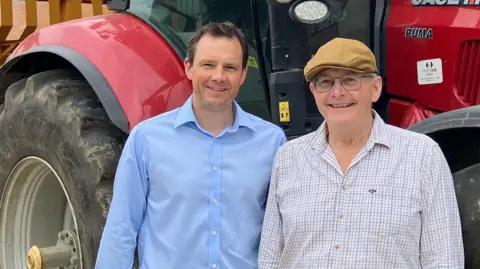 James Marriage and his father Simon Marriage are pictured in front of a red tractor and yellow trailer on the family farm