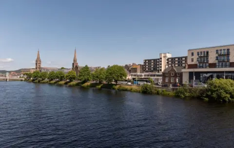 The River Ness flows through Inverness. There are two spires on the bank. 