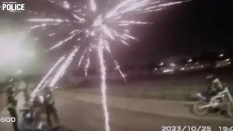Fireworks explodes over heads of police officers standing in road