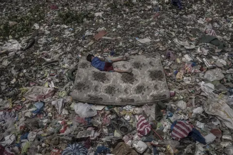 Mario Cruz A boy lies on a mattress amongst rubbish