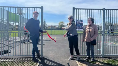 A man and two women cut the ribbon at the opening of the MUGA