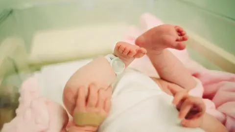 A newborn baby in a hospital ward - all you can see are the baby's feet and a security tag