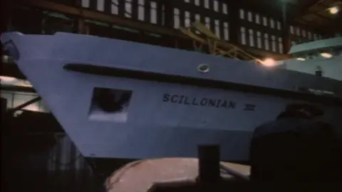 An old grainy 1977 picture of the white hull of Scillonian III in a covered building 