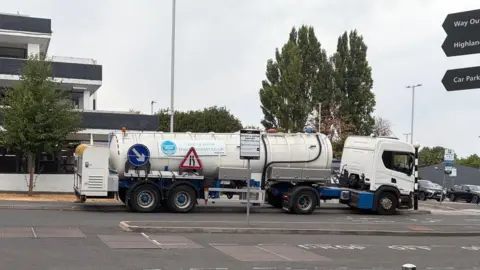 A large white Thames Water tanker is parked outside a grey building belonging to Chase Farm hospital. 