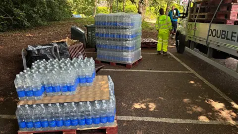 Simon Jones/BBC Several slabs of water placed at a car park. There is a contractor, in a hi-vis clothing, standing beside a lorry. 