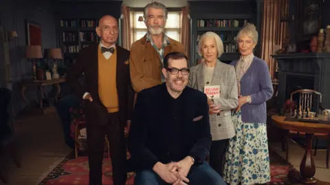 Netflix Richard Osman on the set of The Thursday Murder Club with cast Sir Ben Kingsley, Pierce Brosnan, Dame Helen Mirren and Celia Imrie in costume