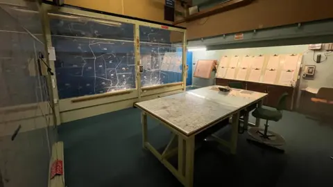 Oli Constable/BBC A room with a table in the middle. On the table is a map of the UK. On the back walls are two maps of northern England, printed onto a clear piece of perspex