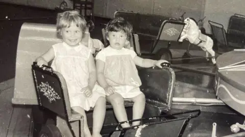Jan Taylor A black and white photo of two young girls sitting on chairs and looking into the camera