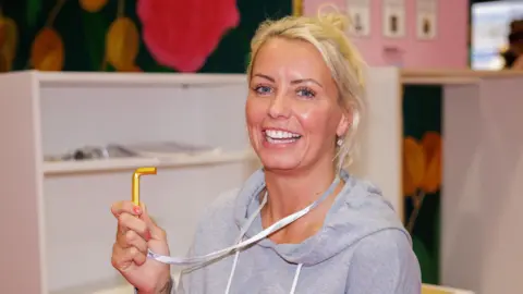 Hayley McAuley who has blonde hair and is wearing a grey hoodie brandishes the golden hex key she won for winning the The Flatpack World Championships,