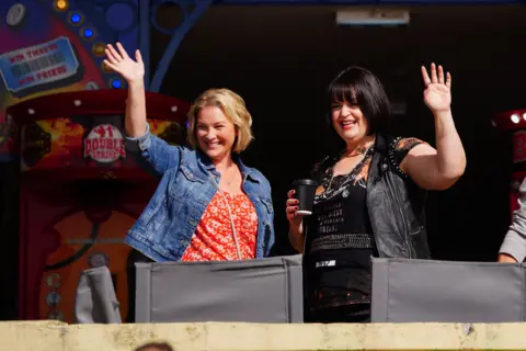 PA Media Joanne Page and Ruth Jones wave to the cameras from outside an arcade on Barry Island, Wales