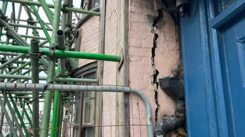 George Carden/BBC A big crack on the front façade of the building. Scaffolding can also be seen propping up the building.