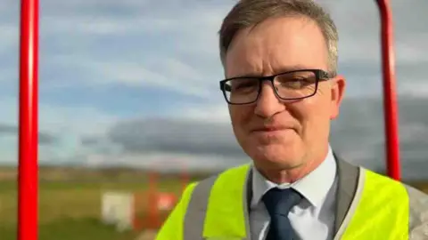 Emma Baugh/BBC Man in yellow hi-vis jacket on A47 site