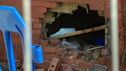 A close‑up of a hole in a brick wall showing broken bricks and debris.
