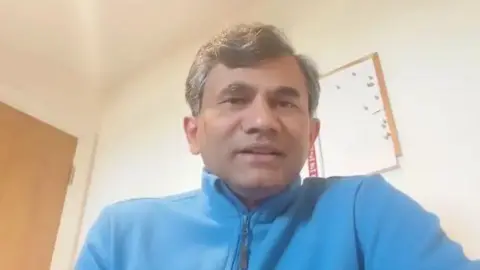 A screengrab of Sangram Patil from a YouTube video, in which he can be seen wearing a turquoise apparel. He is sitting in a room.
