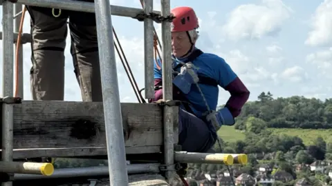 Guildford Cathedral An elderly man prepares to abseil down off a high building.