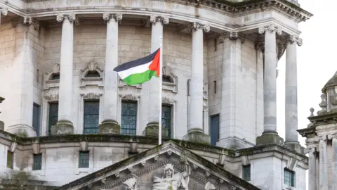 CAOIMHIN MCNULTY/PA Palestinian flag flying from Belfast City Hall. The flag is green, white, red and black. The city hall building is cream stone with engravements and statues.