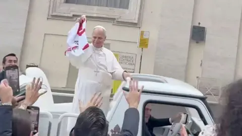 Pope Leo waves the jersey from the pope-mobile