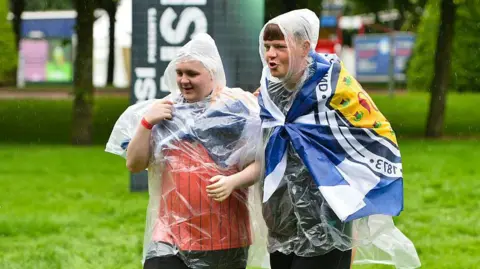 Getty Images Two people arrive at TRNSMT, wearing ponchos over Scotland tops and with Saltires on