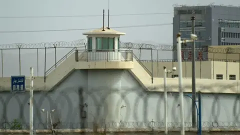 Getty Images This photo taken on July 19, 2023 shows a surveillance tower of an alleged detention center in ARTUX in the Kizilsu Prefecture in the Northwest Region of Xinjiang in China. The high walls covered with spike wire are visible on each side of the detention center