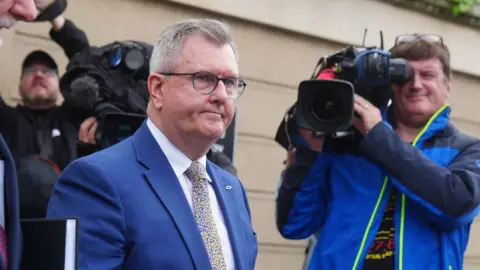Sir Jeffrey Donaldson walks past a cameraman outside court. He is wearing a blue suit