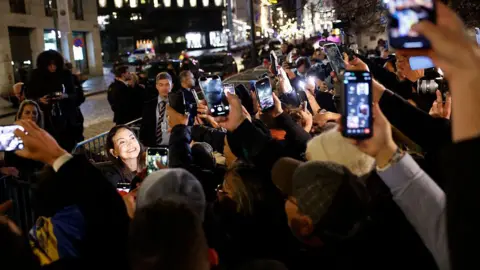 AFP via Getty Images Machado, whose face is illuminated by camera lights, smiles as supporters and media gather to see her arrival.