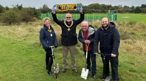 From left: Ann Jones holding a scooter up, Paul Jones holding a skateboard above his head, John McCabe leaning on a spade and Nicholas Beswick holding up a scooter.