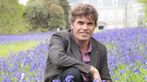 University of Exeter Dave Hodgson knelt in a field of purple flowers. 
