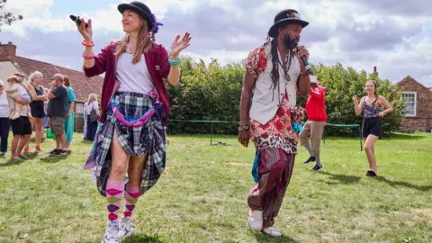 A man and a woman folk dancing on a grassed area. They are wearing colourful clothing. 
