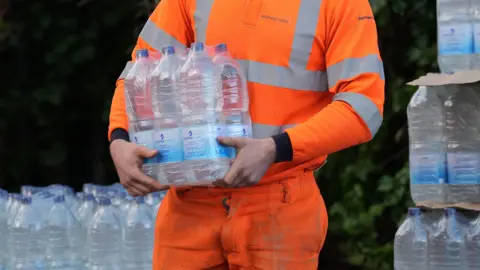 A worker in orange hi-viz hands out bottled water