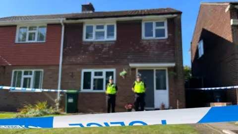 PA Media Police officers in uniform stand in front of a house cordoned off by police