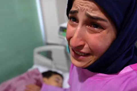 Darren Conway/BBC Najat is crying at her son's hospital bed.