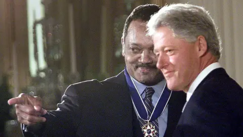 Getty Images Jackson is wearing the presidential medal of freedom while pointing. Bill Clinton is smiling. 