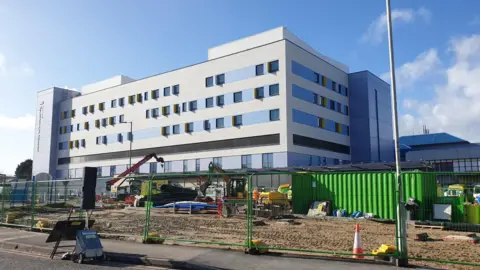 Exterior shot of the BEACH building at Bournemouth Hospital. There are road and landscaping works going on in front of the building as it nears completion.